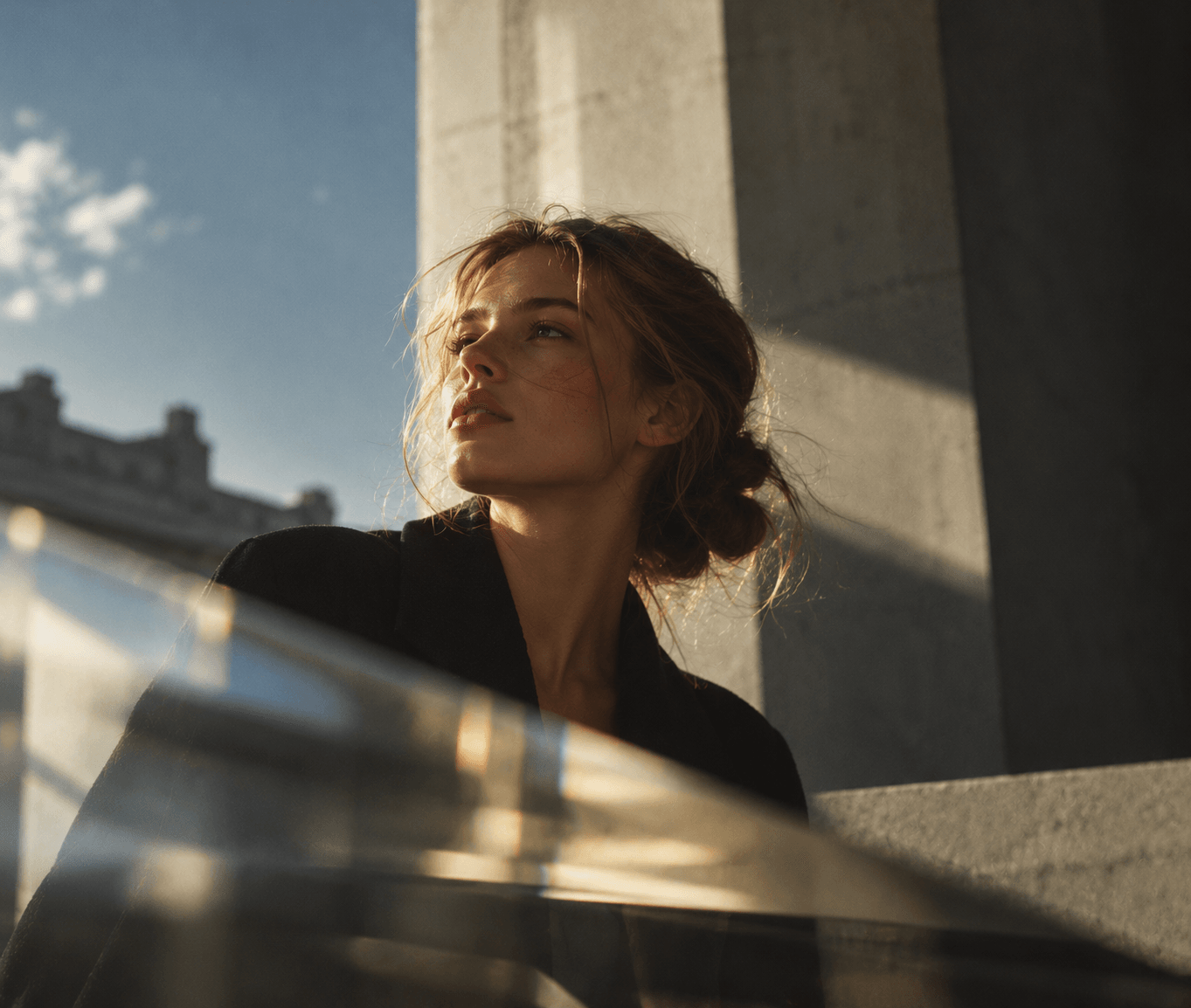 Aurelia in a black coat looking up in warm sunlight beside a stone column